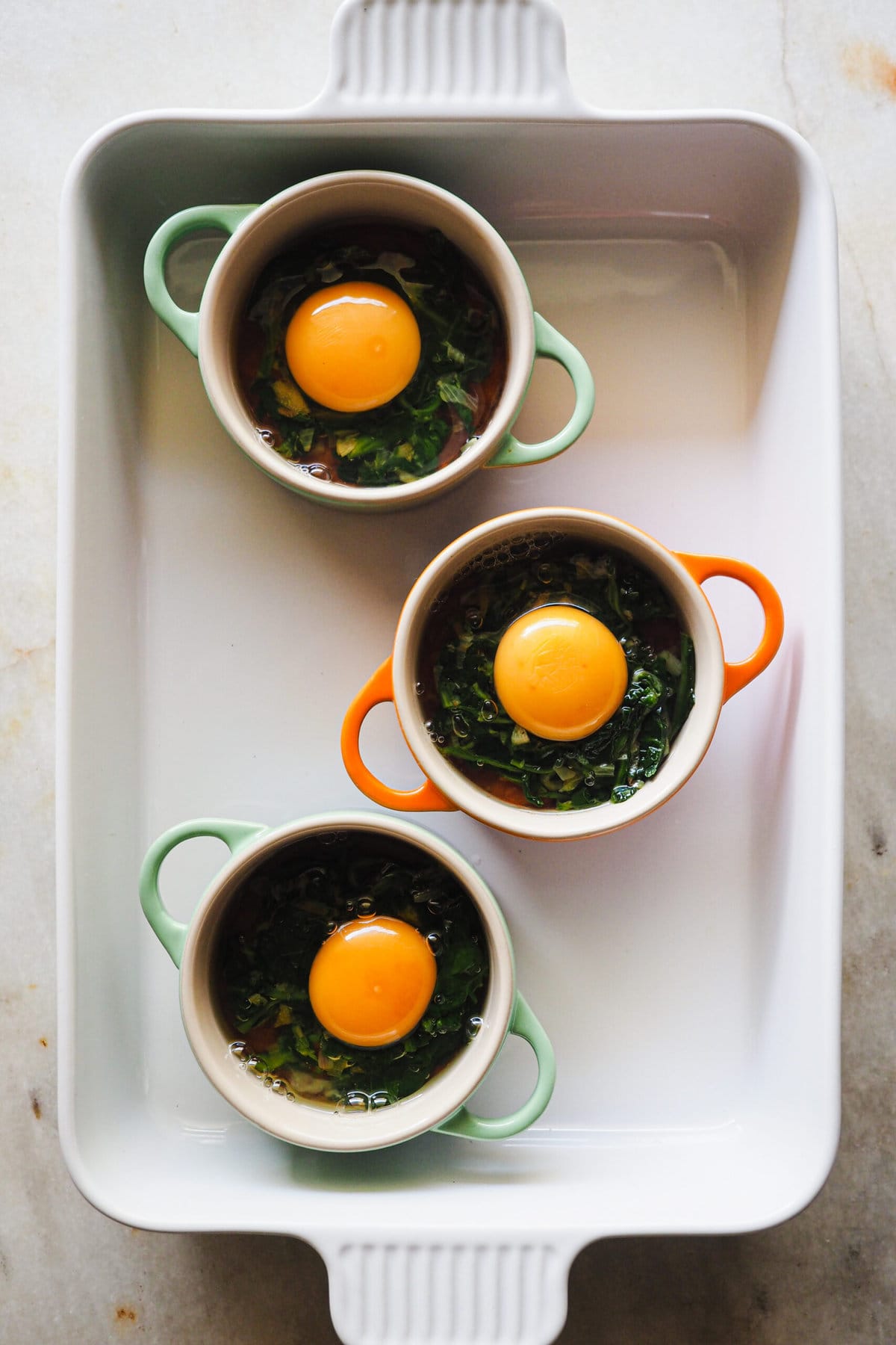 Paula's Apron Huevos en Cocotte con Salsa de Tomate y Espinacas Paso 3 Huevos en Cocotte con Salsa de Tomate y Espinacas: cascar los huevos encima de la base de salsa de tomate y salteado de espinacas.