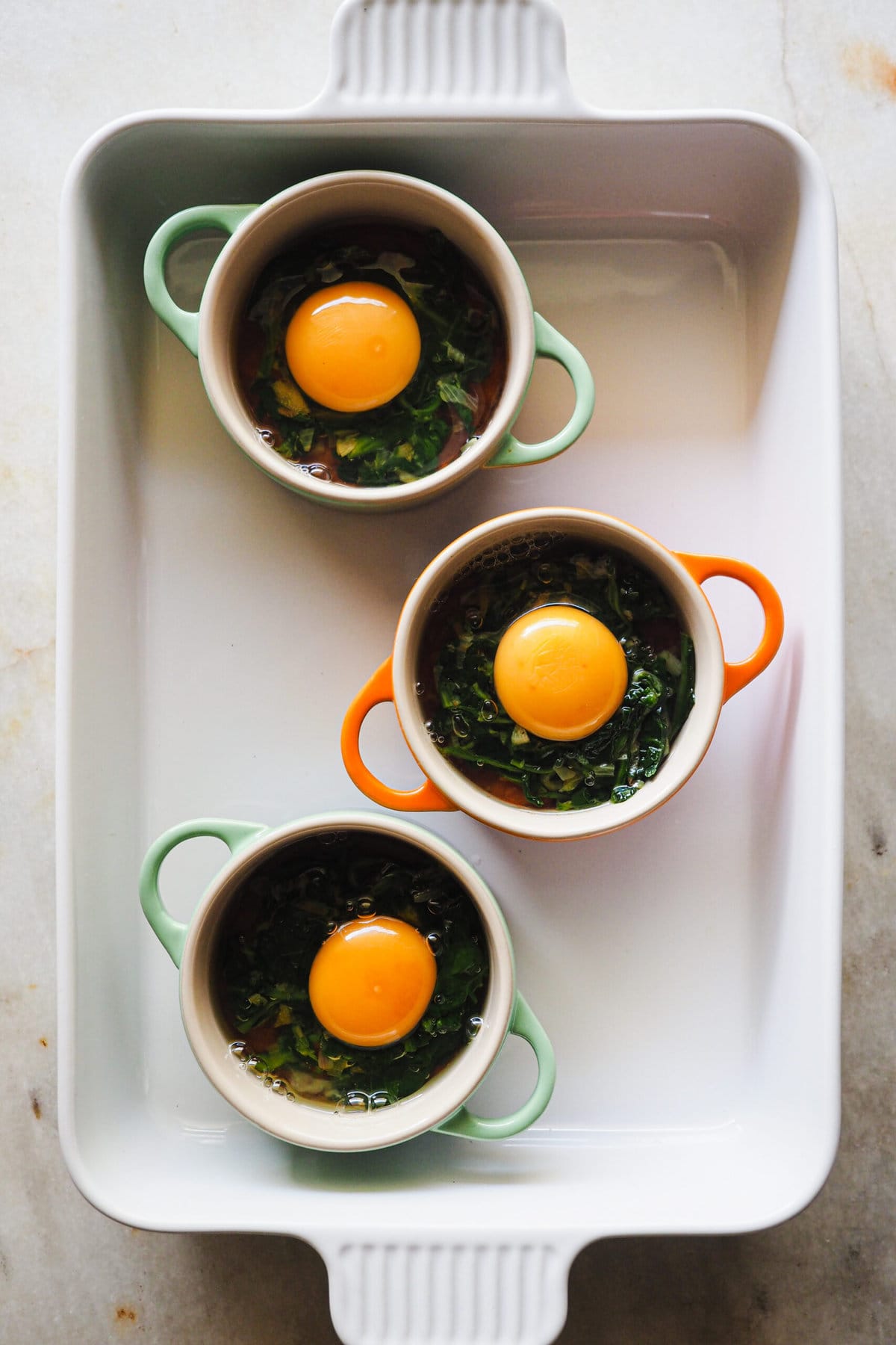 Paso 3 Huevos en Cocotte con Salsa de Tomate y Espinacas: cascar los huevos encima de la base de salsa de tomate y salteado de espinacas.