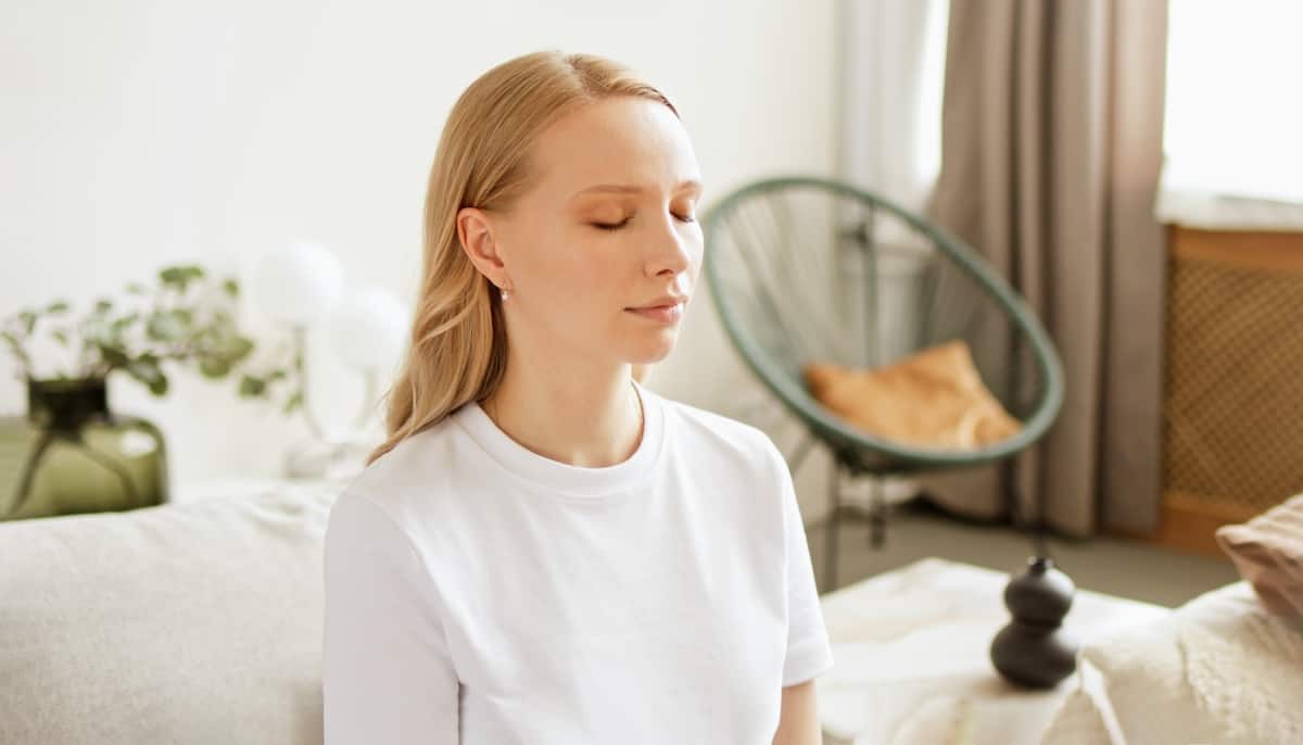 Woman with closed eyes doing breathing meditating practices at home. Making deep breath-exhalation pranayama exercises.