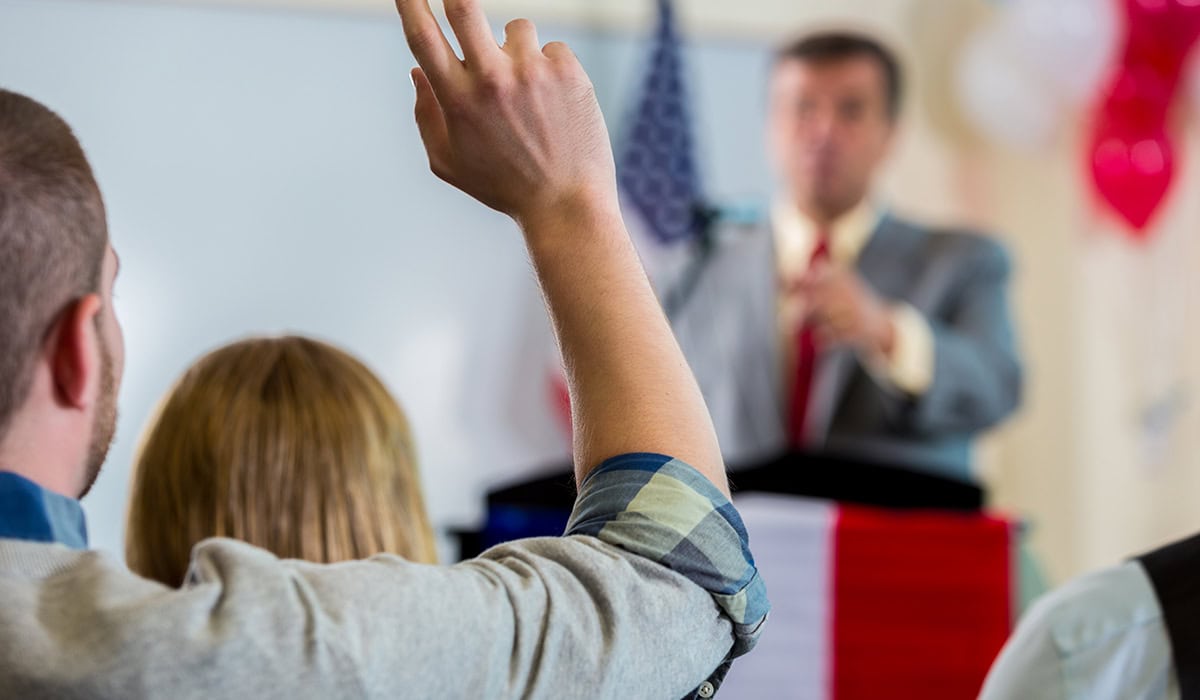 Young Man Raising Hand During Political Town Hall Meeting