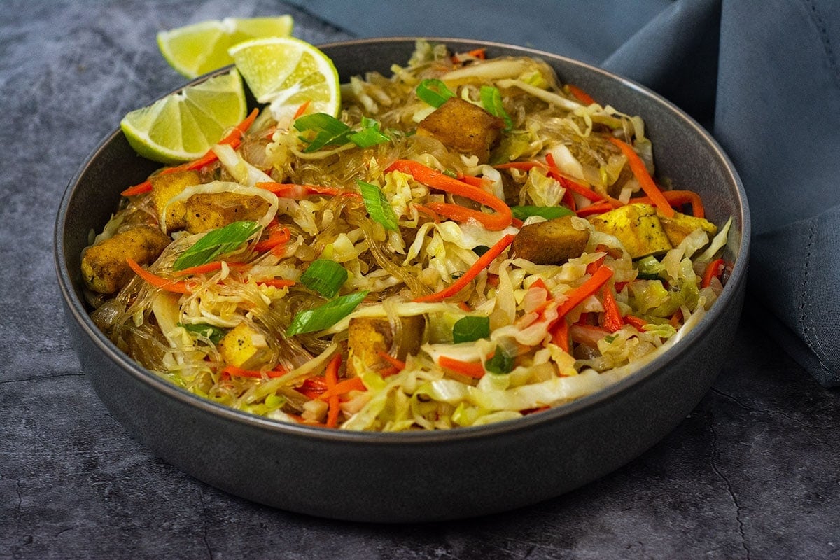 straight on vegan pancit bihon in a grey bowl garnished with green onions and lime on a grey background
