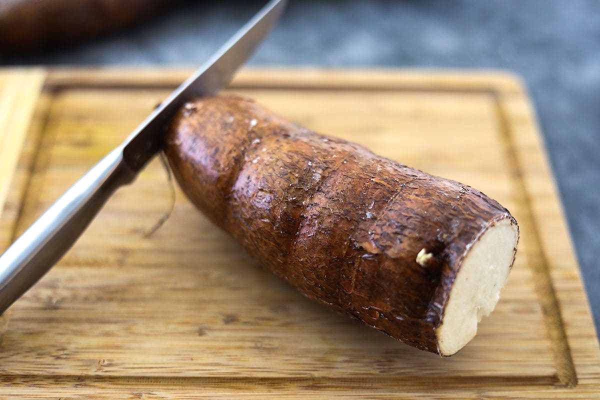 cutting cassava on a cutting board with a silver knife