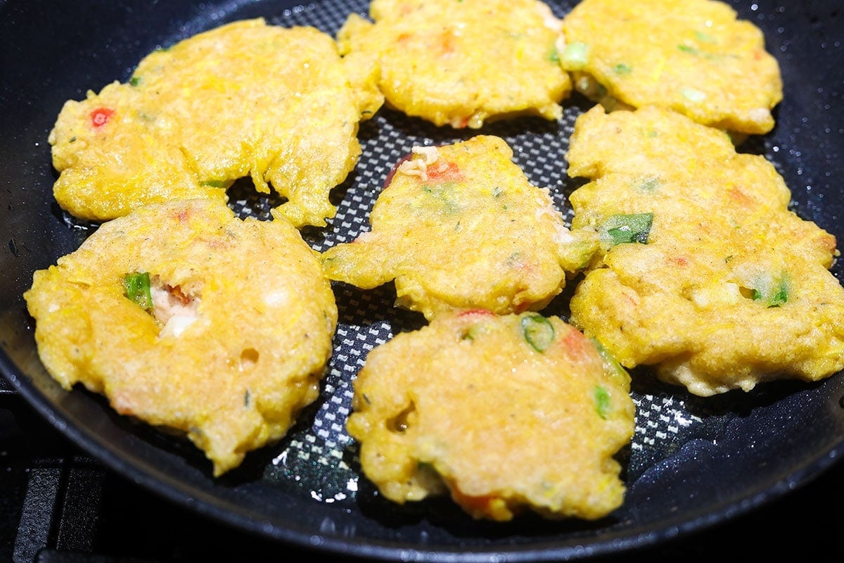 Plantain fritters cooking in a large black skillet