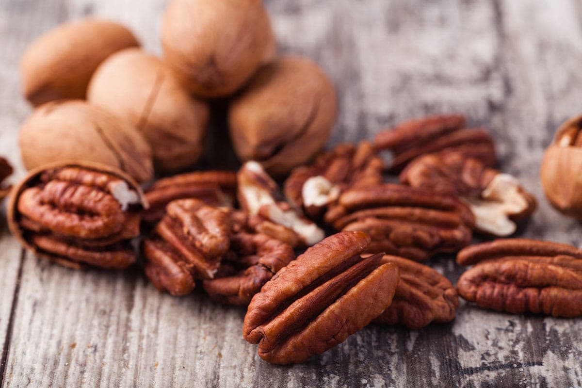 Whole and shelled pecans on a wooden background