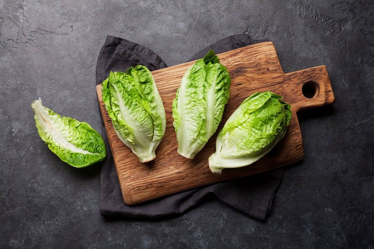 whole bunches of Romaine lettuce on wooden cutting board on a grey background