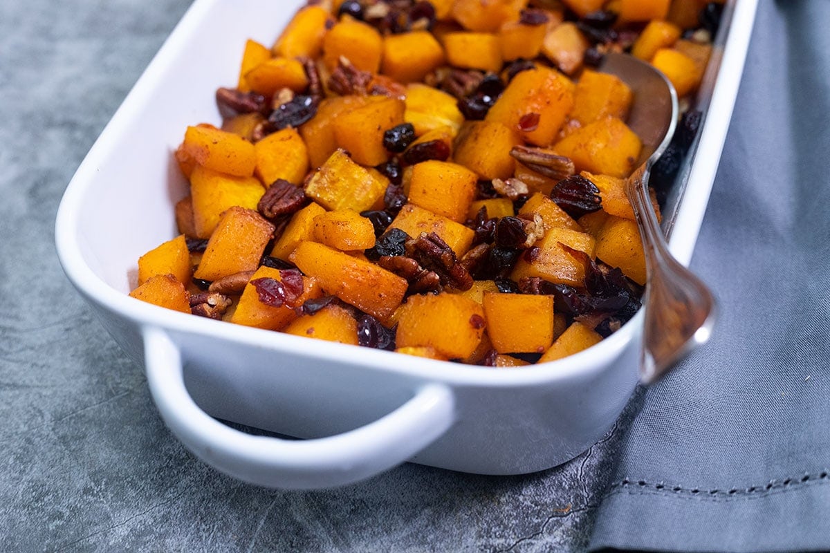 roasted butternut squash with cranberries and pecans in white dish on a grey background