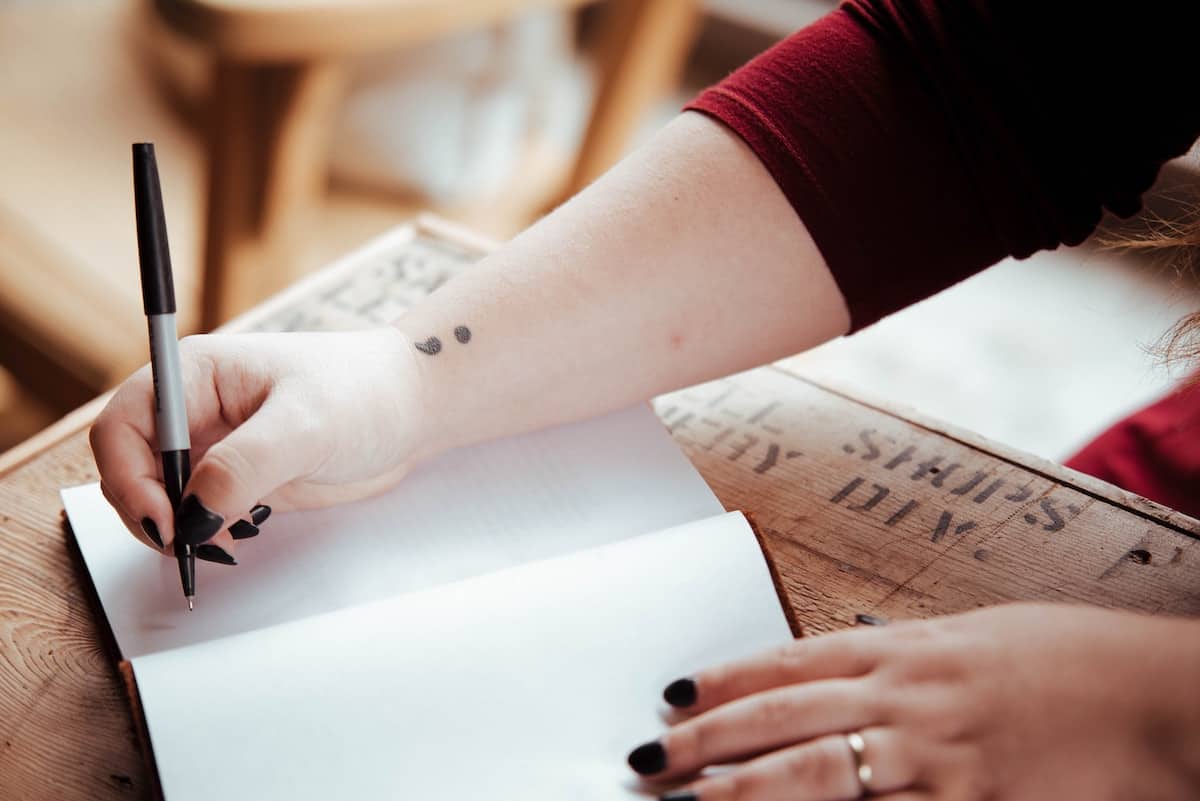 woman writing in journal with semi colon tattoo on wrist