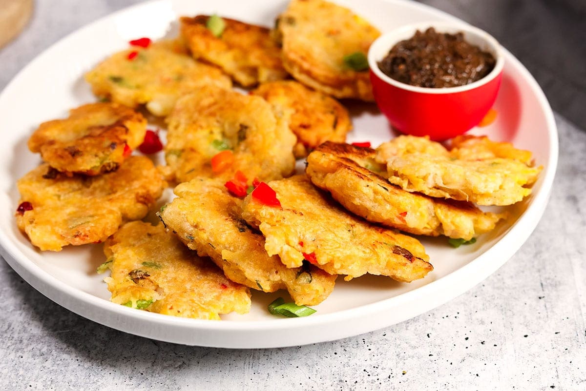 Plantain fritters close up in a white plate with a small bowl of jerk dipping sauce