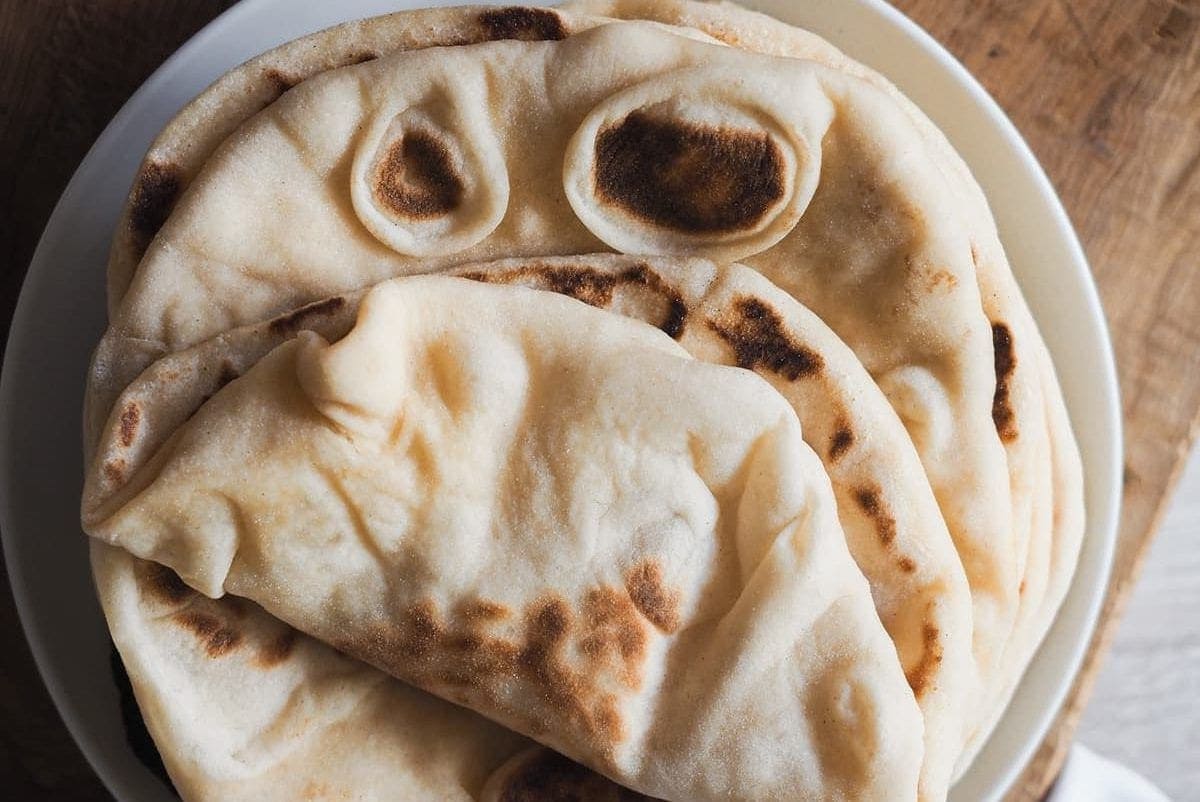 This delicious, pillowy soft Turkish Flatbread is simply incredible! It’s extra soft, tender and hollow, a perfect cross between Naan bread and Pita bread. Serve alongside your favourite saucy dishes, with grilled meats, hummus, or simply on its own. Overhead shot of a plate with a few bazlamas. The one at the very top is folded.