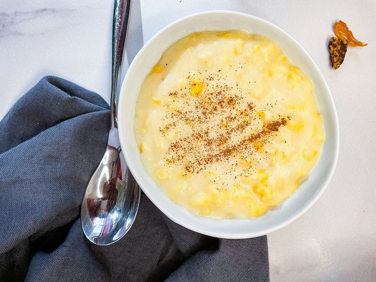 overlay of hominy corn porridge on a white background with a grey napkin spoon, and nutmeg