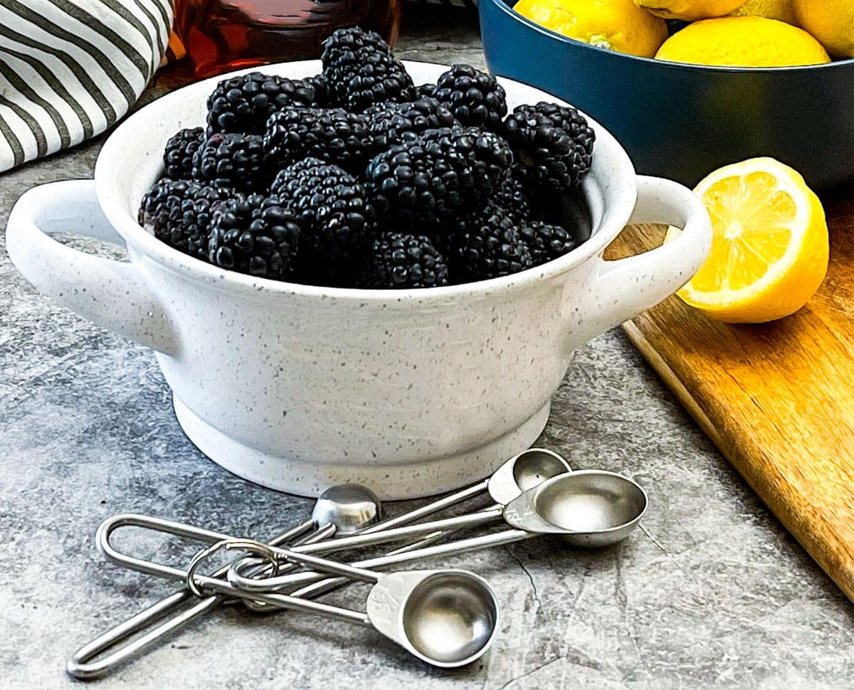 blackberry lemonade ingredients in a white bowl and lemons on a cutting board on a grey background