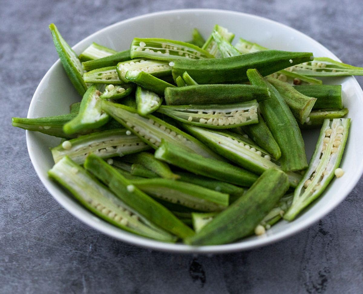Okra cut in half lengthwise in a white bowl