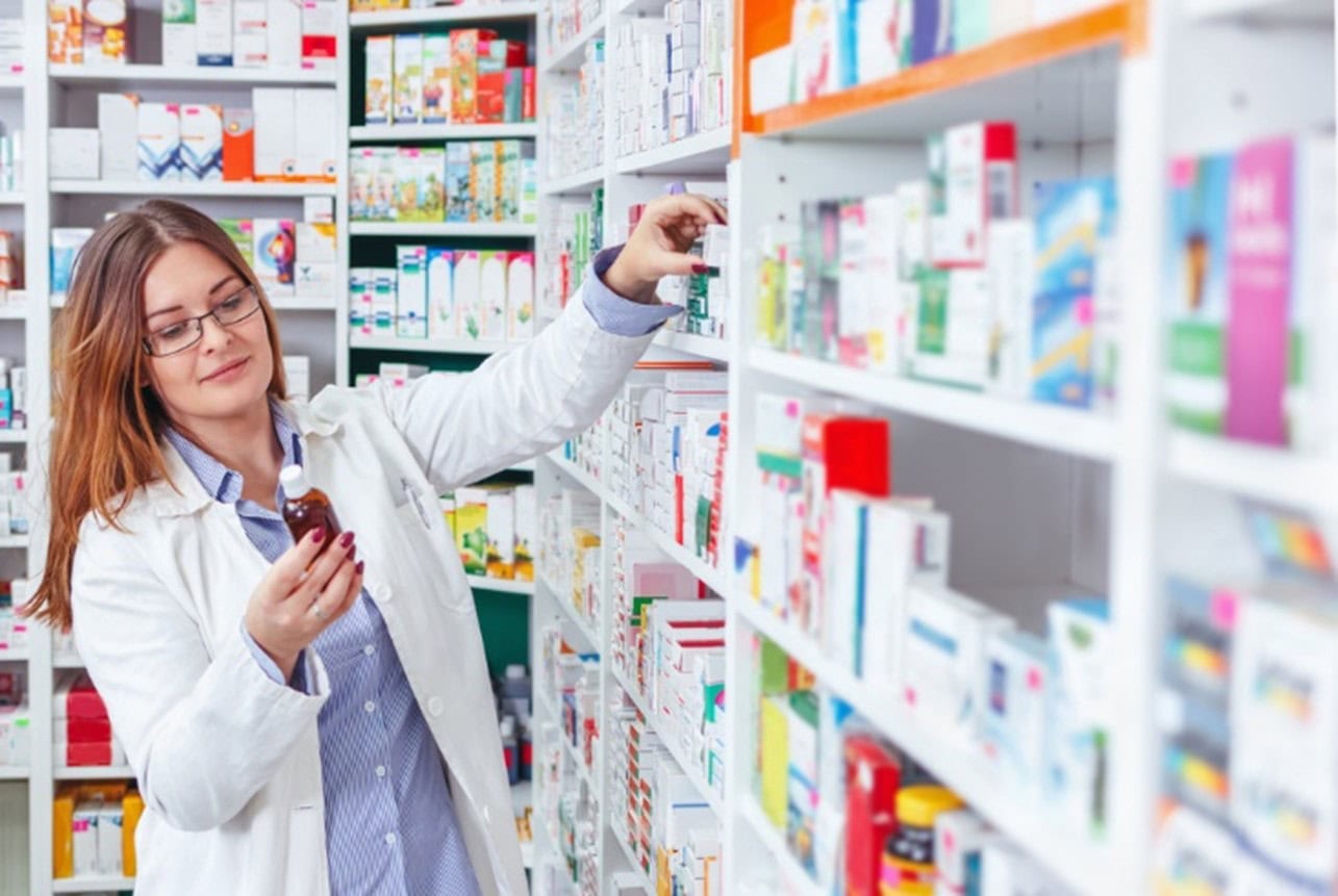 Farmacêutica conferindo um medicamento na prateleira da drogaria