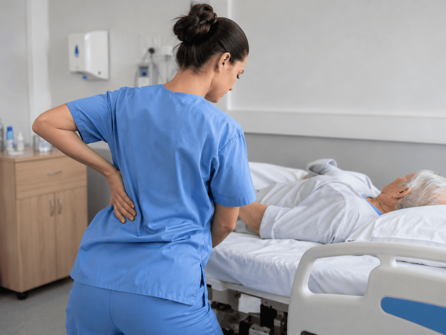 Nurse with back pain repositioning an elderly patient in a hospital bed