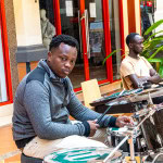 Musician playing a drum kit while another musician sits behind him