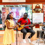 Woman singing beside a seated bass guitarist and drummer
