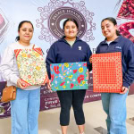 Three smiling participants display colourful finished fabric panels at the Frame and Fabric Workshop.