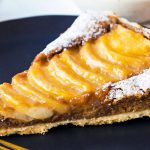 Closeup up of plated pear frangipane tart piece with sliced pears on top glazed with apricot jam