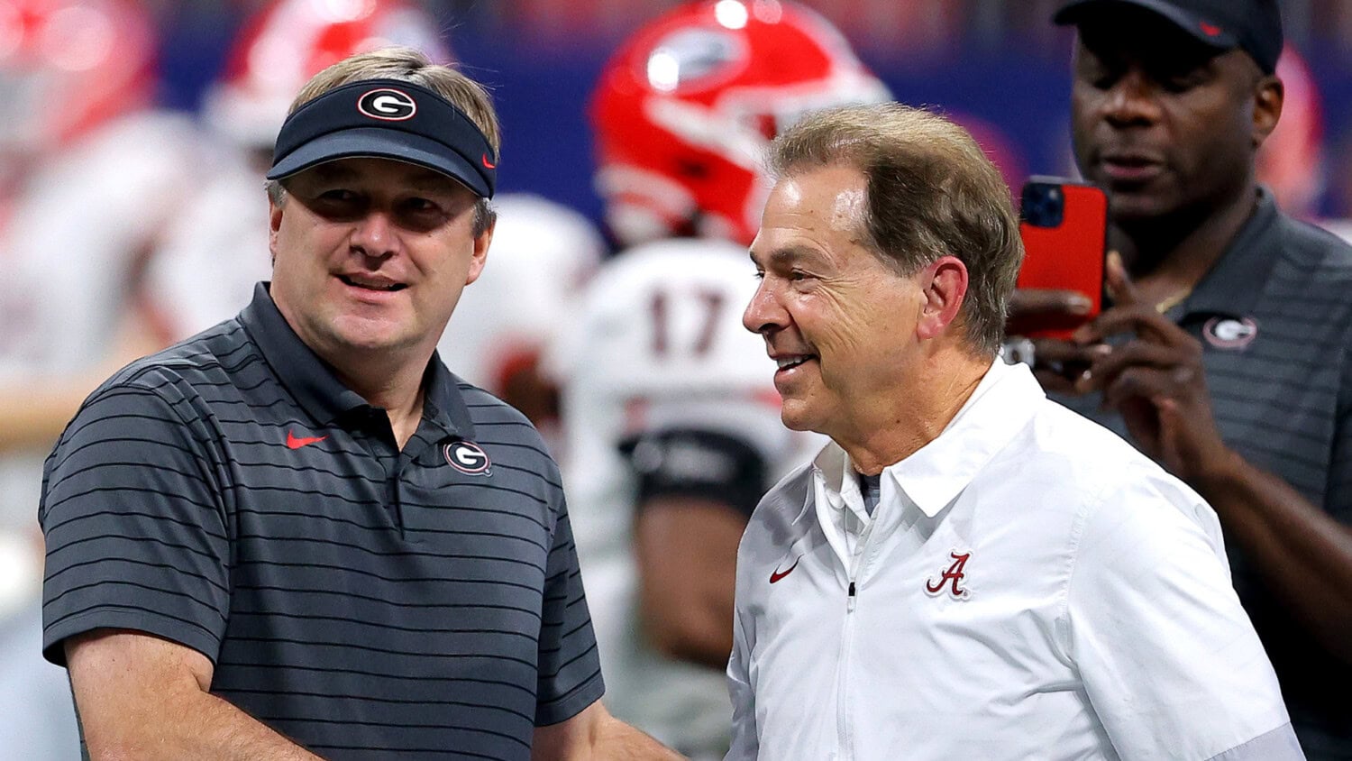 Kirby Smart and Nick Saban shaking hands and smiling on the sideline before a football game