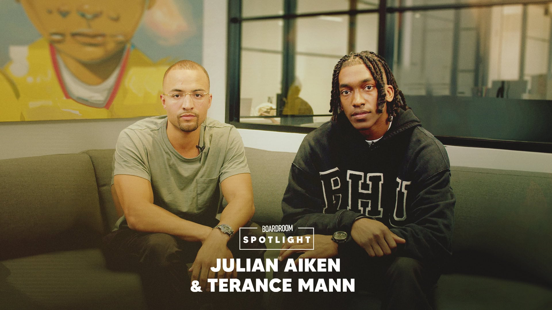 Terrance Mann sitting on a couch next to Julian Aiken in front of a glass window