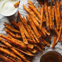 Boniatos Fritos al Horno, perfectos como aperitivo otoñal, guarnición o como pica pica si haceís plan para ver deporte con amigos por ejemplo. Son más saludables que si los hacemos fritos, súper fáciles y quedan realmente crujientes! Los acompaño con un dip de mayonesa especiada que puedes hacer picante o no al gusto. Aquí se ven los boniatos sobre papel con cebollino, sal y dispuestos entre dip de mayonesa con un boniato dentro, cerveza y guindilla en copos.