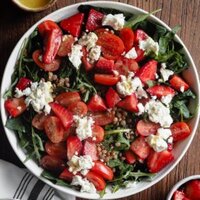 This colourful Spinach Strawberry and Feta Salad with Lentils is easy, packed with good things and filling thanks to the pulses. The lemony punch of the Lemon Mustard Dressing that goes with is simply amazing. In this overhead shot the salad can be seen served on a plate in the centre of the shot. At the top left corner there's a pinch bowl with more dressing, at the bottom right corner there's a little bowl with strawberries and at the bottom left corner there's a kitchen cloth with 2 silver spoons over it.