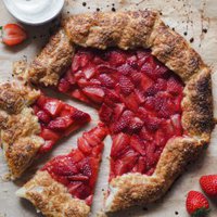 Esta Galette de Fresas con Nata Avainillada es espectacular! Hecha con un hojaldre rápido y acompañada con nata avainillada montada, es una variación del clásico postre de fresas con nata que dejará a todo el mundo flipando. En esta foto se ve toda la galette, con 2 porciones cortadas y un poco separadas del resto de la galette. Arriba a la izquierda hay un pequeño bol con nata, media fresa encima y media fresa a su lado izquierdo. Abajo, a la derecha de la galette hay 2 fresas.