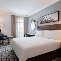Svetla hotelska soba sa velikim krevetom, foteljom i zavesom na prozoru
