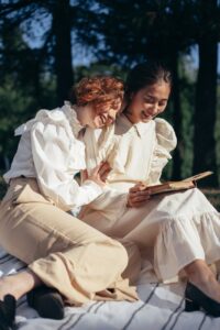 Celebrate Pride Month with These 9 Fabulous Date Night Ideas for the LGBTQIA+ Community 9 smiling women in old fashioned clothing reading book on picnic blanket