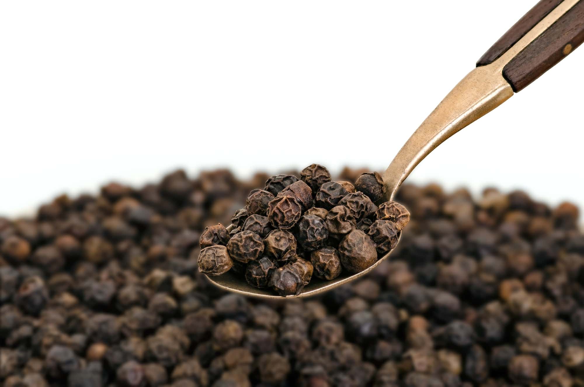 Whole Black Pepper on Old Brass Spoon