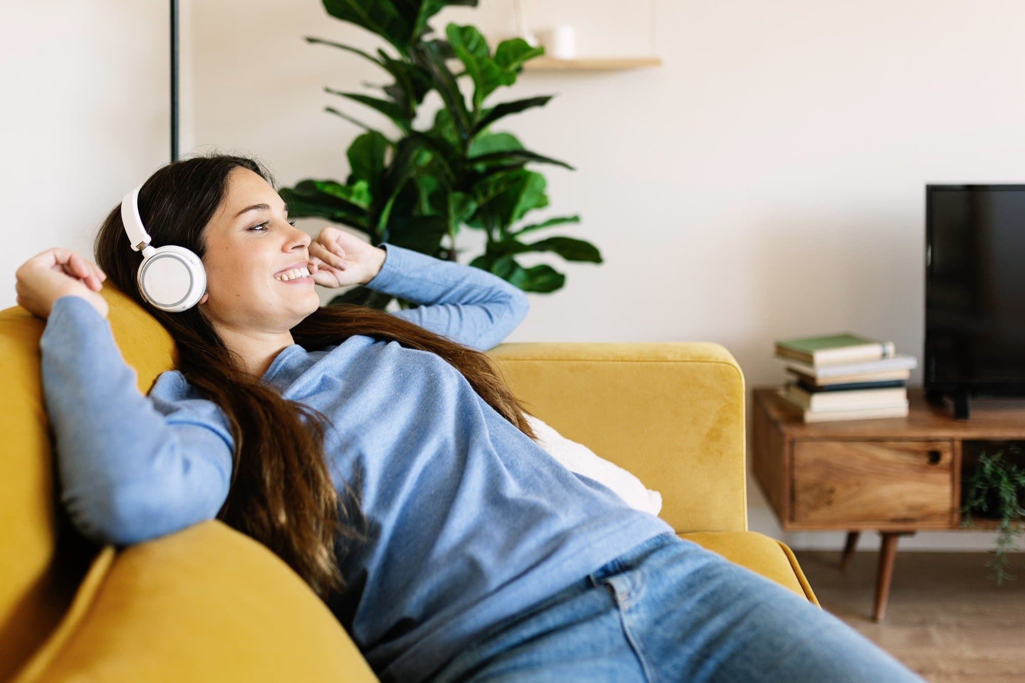 Relaxed smiling young adult woman with headphones sitting on sofa at home