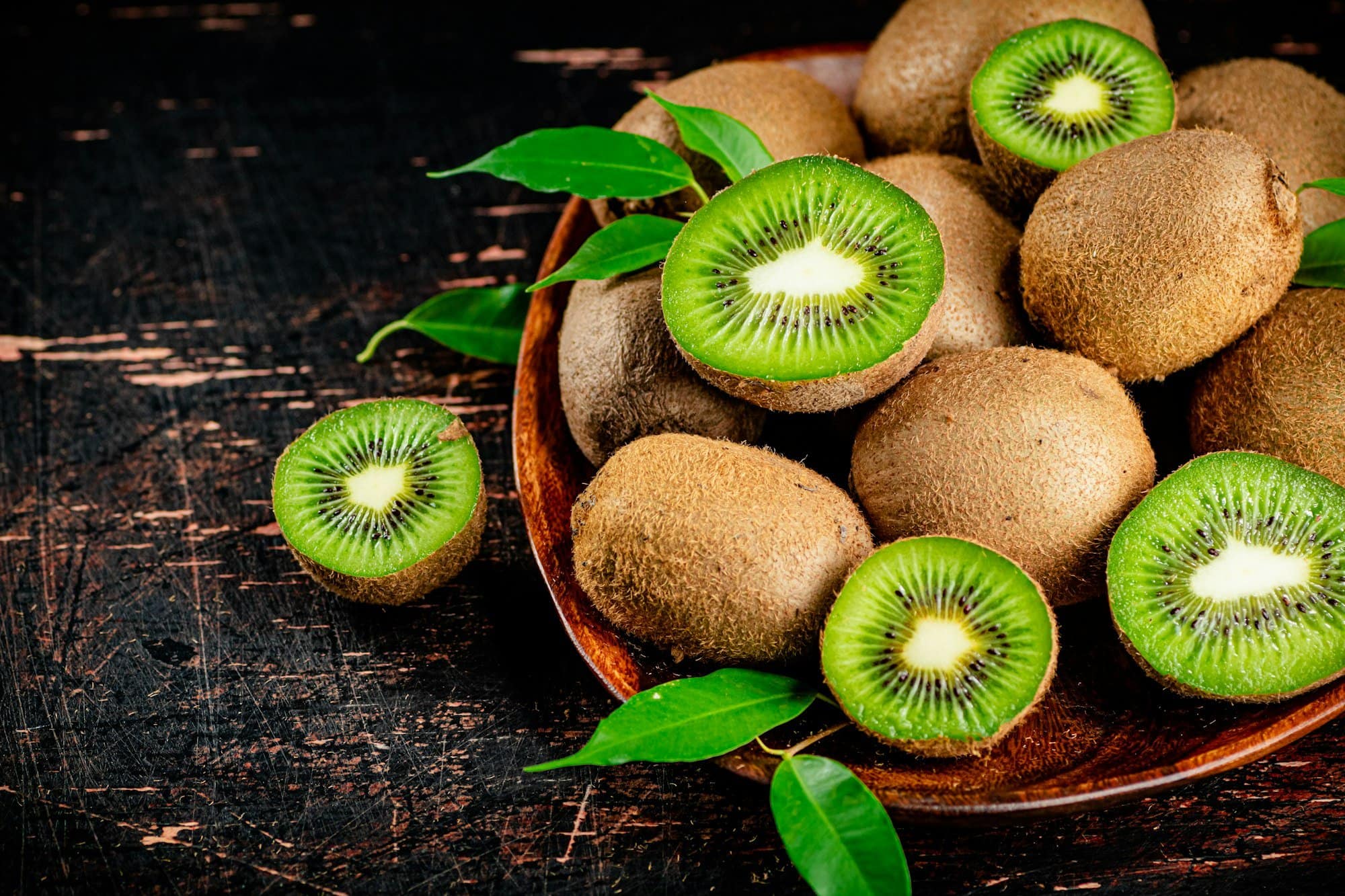 Fresh kiwi with leaves on a wooden plate.