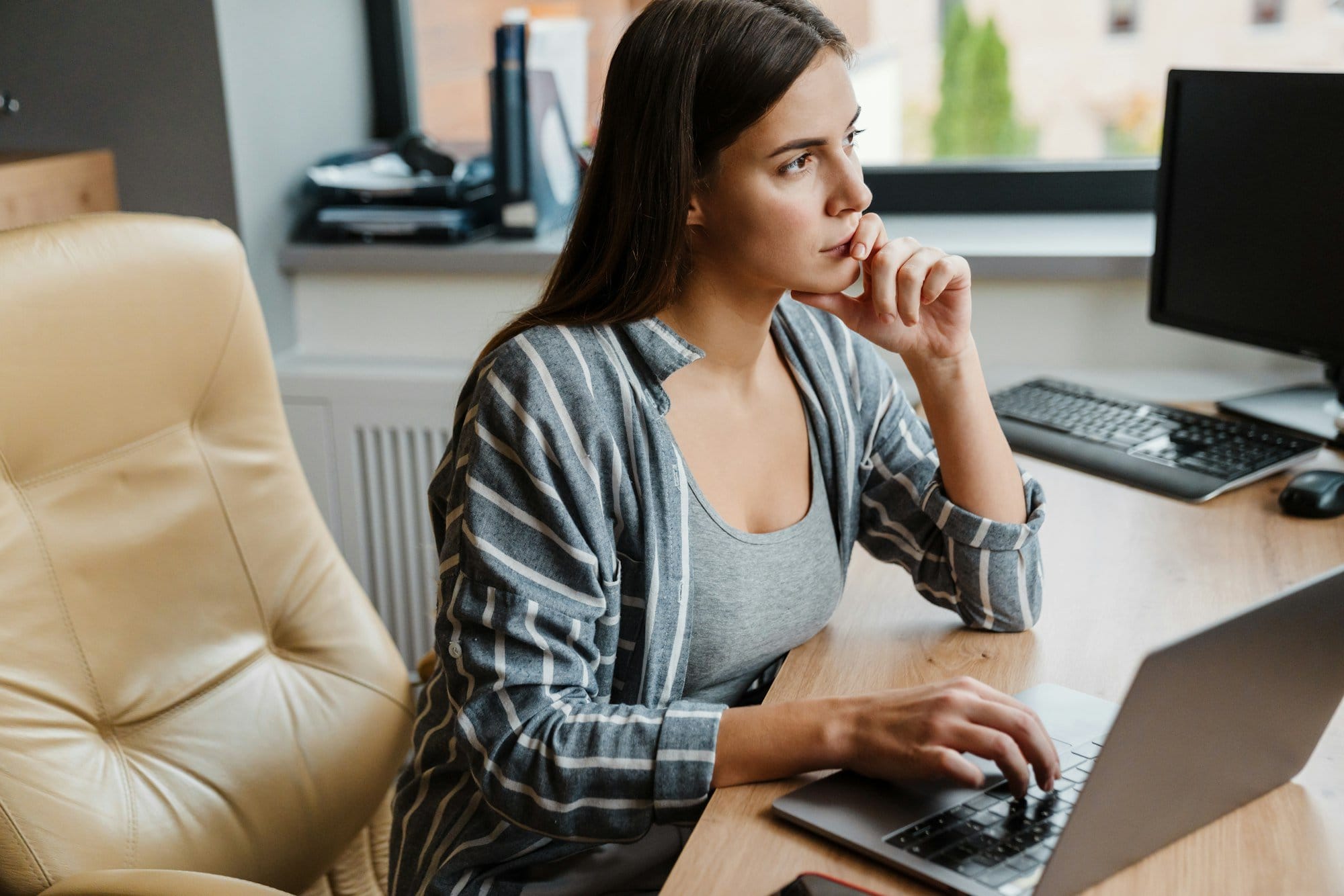 Charming thinking woman working with laptop while sitting at table