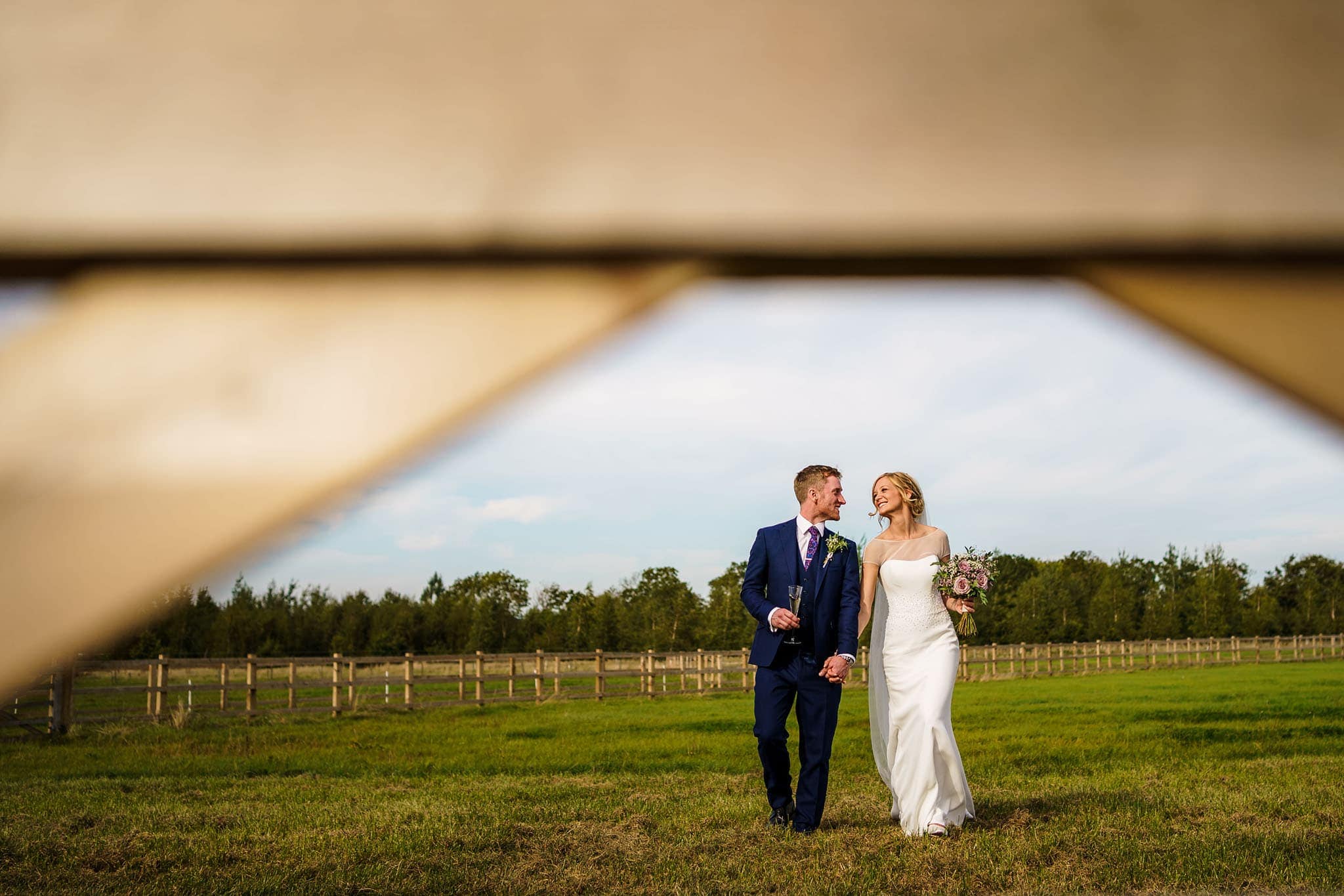 a smiley bride and groom walking together across a field