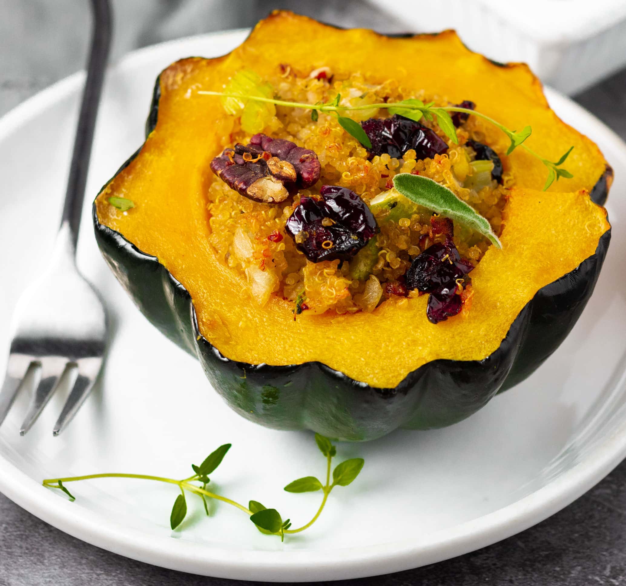 Vegan Stuffed acorn squash on a white plate stuffed with quinoa, cranberries, pecans, and sausage with a black fork