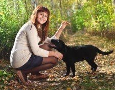 Young lady crouched in the woods saying hello to a black lab puppy