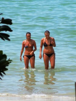 Dve kupačice gaze kroz plitku tirkiznu vodu na peščanoj plaži