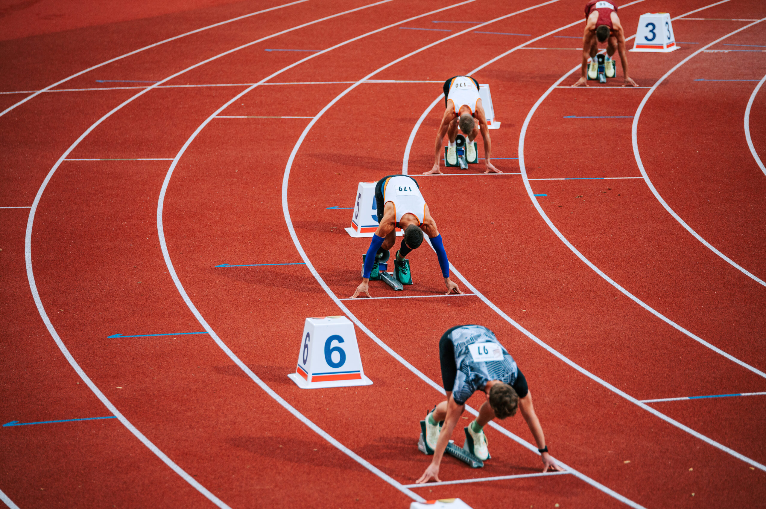 Powerful image of male athletes at the starting line of a 400m race on track. Suitable for sports and fitness campaigns, highlighting determination and focus Powerful image of male athletes at the starting line of a 400m race on track. Suitable for sports and fitness campaigns, highlighting determination and focus