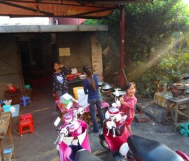 Deca i žena stoje pored uličnih tezgi za pripremu hrane u dvorištu sa motociklima