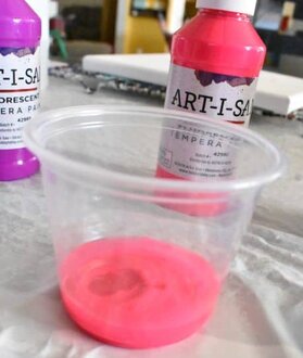water poured into tempera paint in clear plastic cup