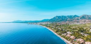 aerial photo of aquamarine water on white sand beaches showing how going to the beach is one of the best things to do in Marbella,with mountain rising in the distance