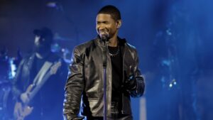 Usher looks to his right and smiles while performing musi in front of a microphone