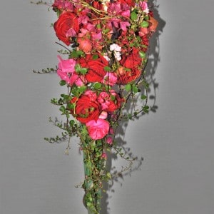 Tropfenbrautstrau&szlig; in Rot-Pink. Strengabflie&szlig;end gearbeiter Strau&szlig; aus roten und pinkfarbenen Rosen, pinken Hortensiendolden und einigen Lavendel Akzenten, umspielt von gr&uuml;nen M&uuml;hlenbeckiaranken.