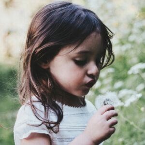 young girl in nature blowing on dandelion flower
