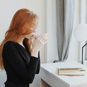 redhead girl drinking a hot drink at desk while journaling