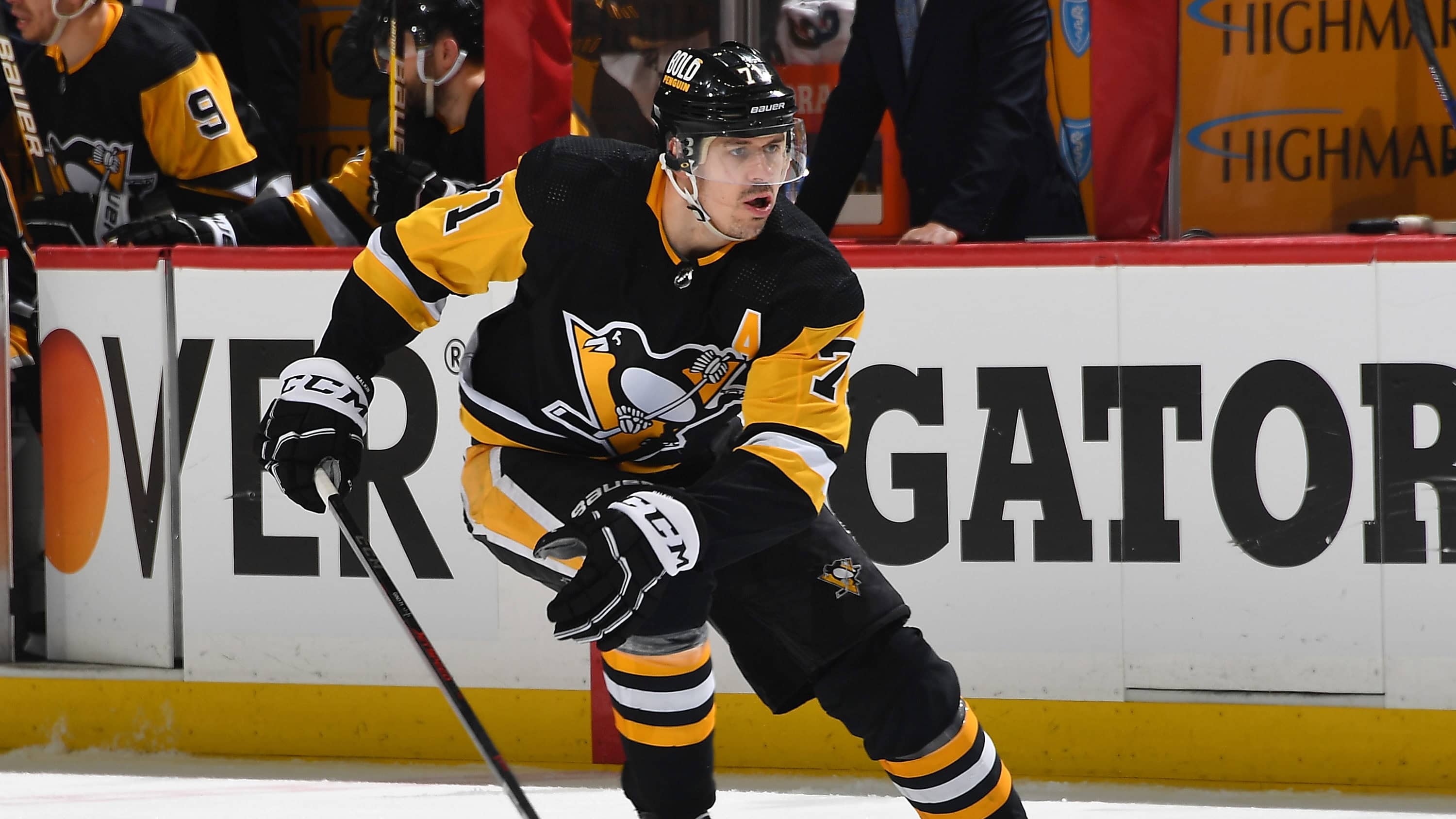 Evgeni Malkin skating on ice holding a hockey stick in his right hand while looking ahead