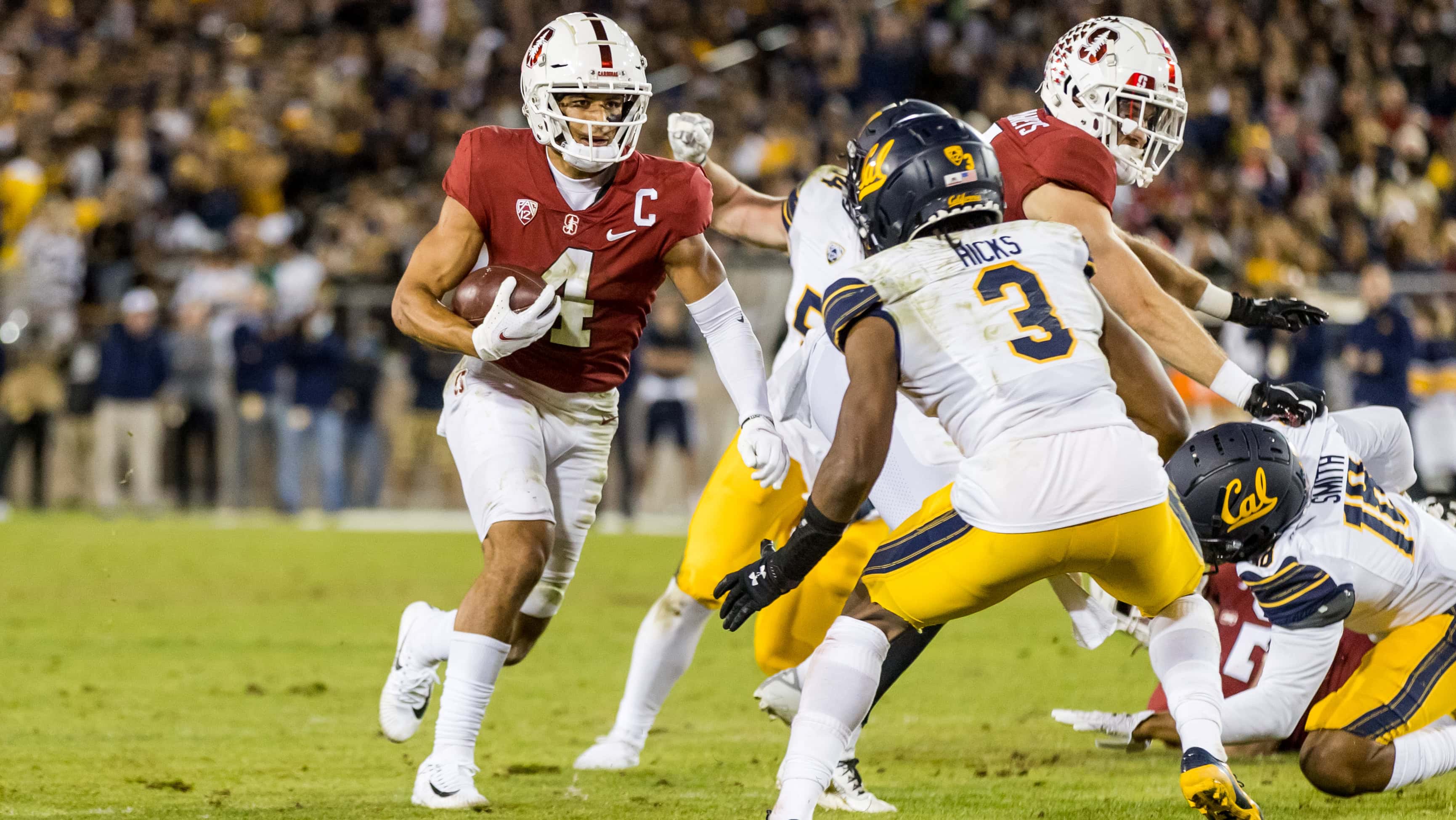 Football player Michael Wilson running with a football cradled in his right arm while an opposing player prepares an attempt to tackle him