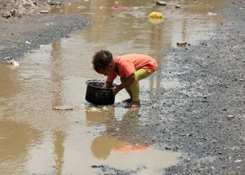 A boy washes a cooking pot in a rain water pool outside a slum area for the Muhamasheen (marginalized) community in Sanaa, Yemen July 26, 2020. Picture taken July 26, 2020. REUTERS/Khaled Abdullah - RC2W2I9BRGSW