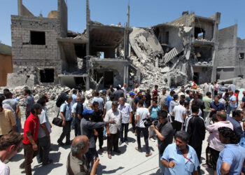 Journalists and locals gather next to the rubble of buildings in Tripoli, Libya, on June 19, 2011. During a governmennt-led tour, the group was shown damaged houses and the bodies of civilians said to have been killed in a NATO coalition bombing. MAHMUD TURKIA/AFP via Getty Images