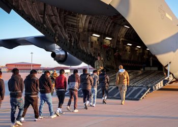 Men in shackles being led on to a military plane. Pic: X/PressSec